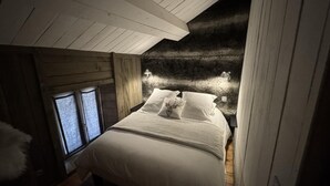 A bedroom with a sloped ceiling, a bed with white bedding, and two bedside lamps. - Gîte Sylvestre - LLO - Gîte (LLO)