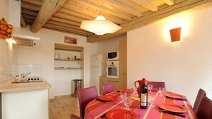A dining area with a table set for four, a wine bottle, and a microwave in the background. - Les oliviers - THUIR (THUIR)