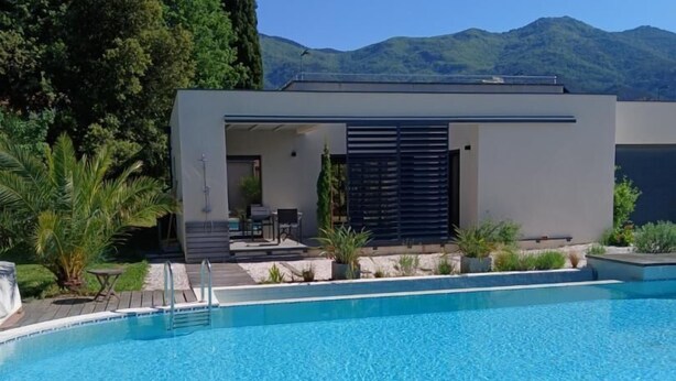 Un área de piscina moderna con una piscina azul cristalina, una pequeña zona de estar al aire libre y un edificio con techo plano y grandes ventanales.