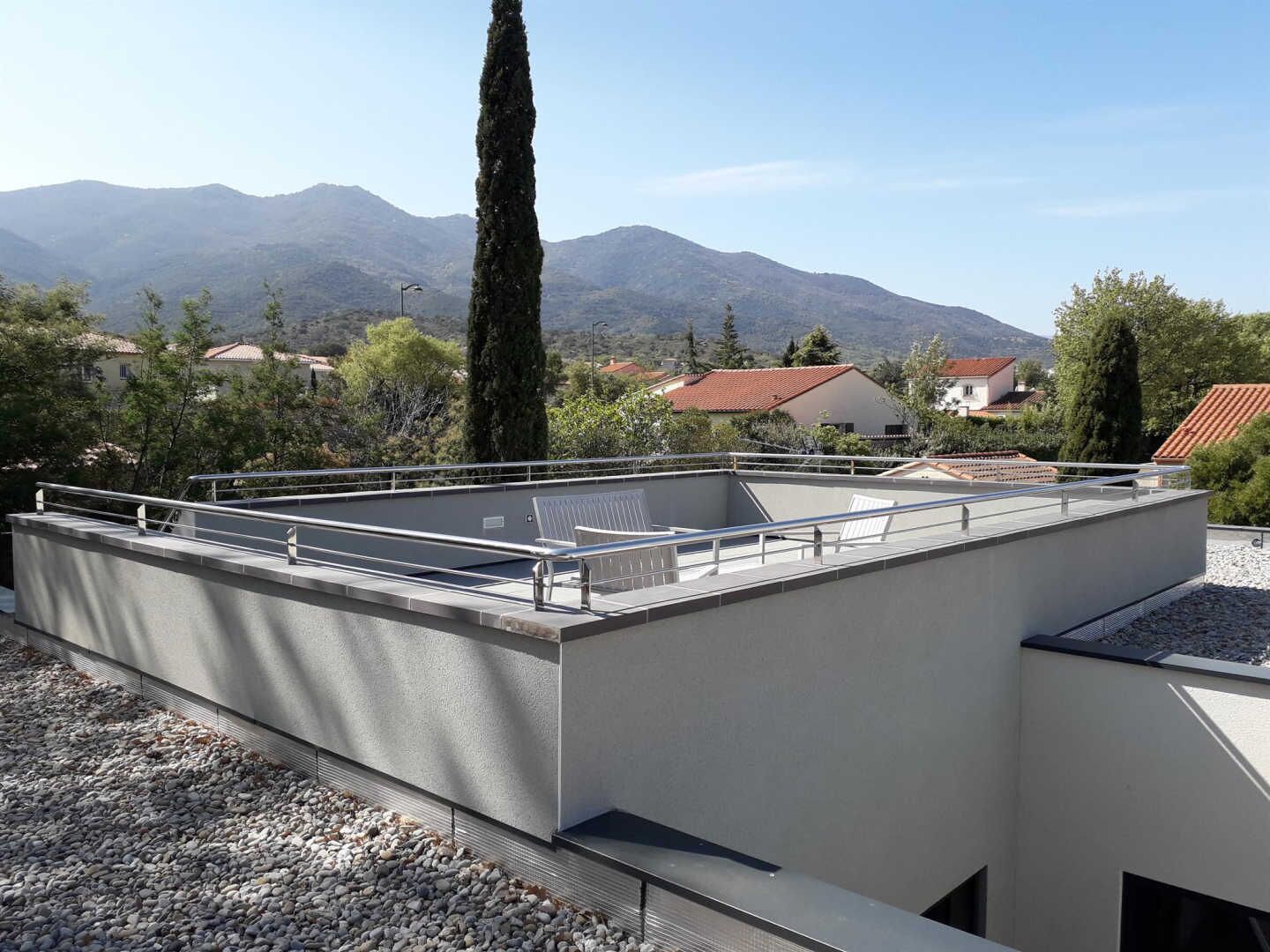 Une terrasse sur le toit, dotée d’un toit plat, d’une rambarde en métal et offrant une vue sur les montagnes et les maisons au loin.