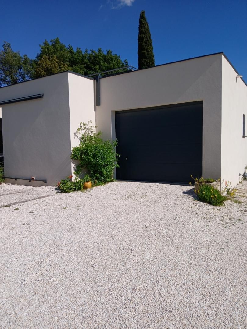 A modern two-story building with a flat roof, a large garage door, and a gravel driveway.
