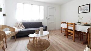 En moderne stue med en grå sofa, fletstole, et rundt sofabord og et spisebord dækket til to personer.