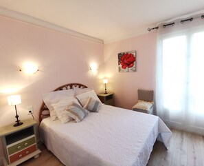 Une chambre à coucher comprenant un lit, des tables de chevet, une commode, une chaise et une fenêtre avec des rideaux.