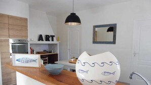 A modern kitchen with wooden cabinets, a black pendant light, a white vase with blue wave patterns, and a fish-shaped container.