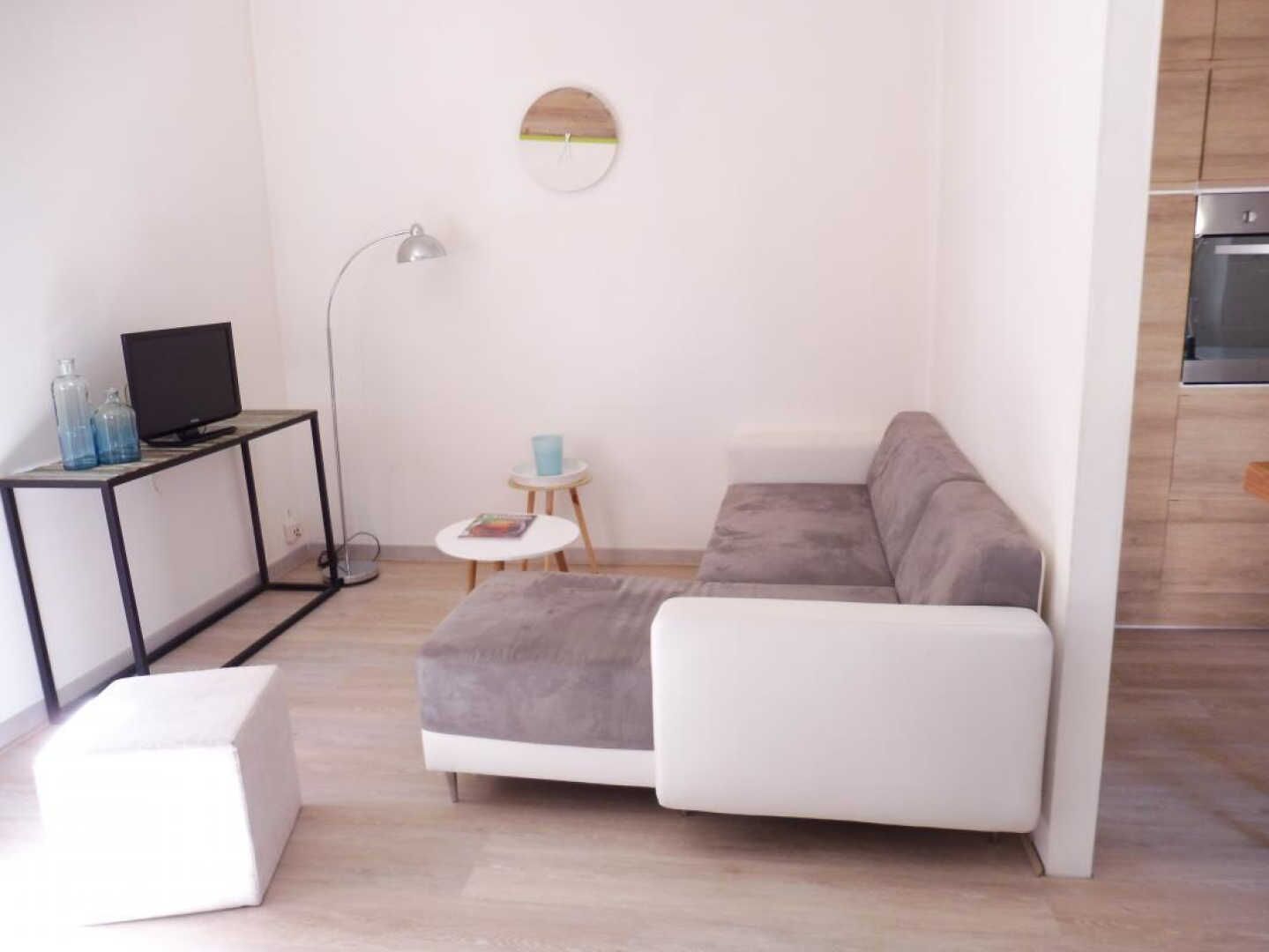 A modern living room with a sectional sofa, a small white table, a floor lamp, and a TV on a black stand.
