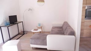 A modern living room with a sectional sofa, a small white table, a floor lamp, and a TV on a black stand.