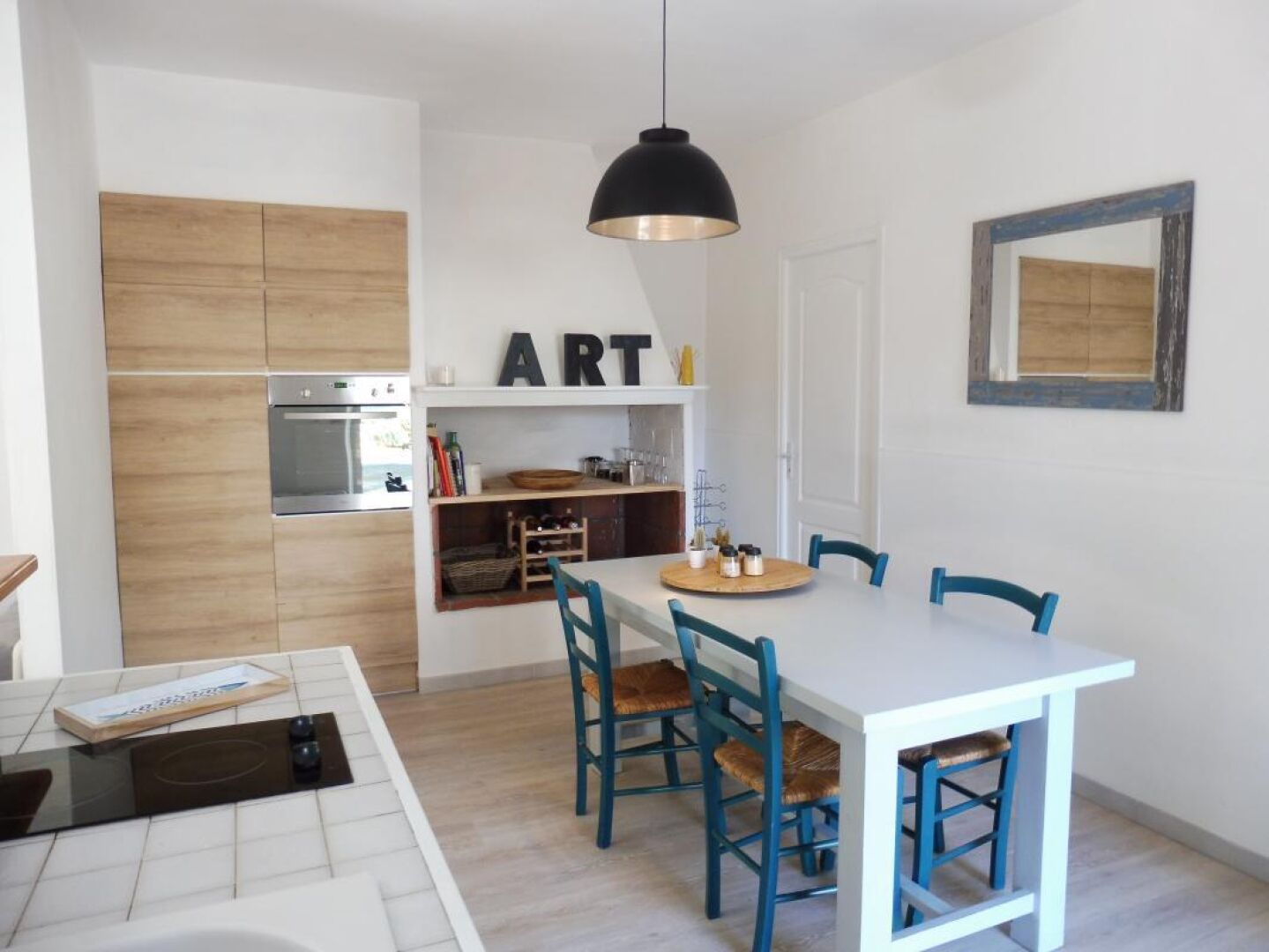 A modern kitchen with a built-in oven, a dining table with chairs, and a pendant light.