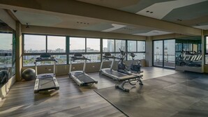 Ein modernes Fitnessstudio mit Laufbändern, Crosstrainern und Fahrrädern. Große Fenster bieten Blick auf die Stadt.