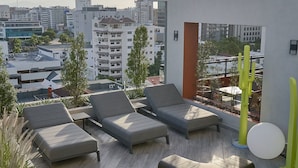 Eine Dachterrasse mit mehreren Sitzbereichen, darunter Sofas und Sessel, und Blick auf die Stadtlandschaft.