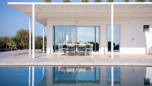 Un área de comedor exterior moderna con una piscina al frente.