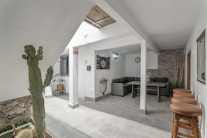 A spacious living area with a high ceiling, a dining table, a sofa, and a cactus plant.