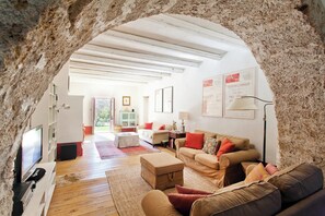 Ein gemütliches Wohnzimmer mit einem Steingewölbe, Holzböden, einer Sofagarnitur, einem Fernseher und gerahmten Postern an der Wand.