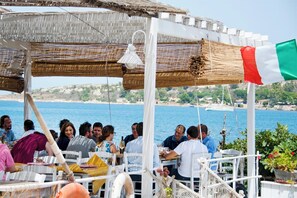 A covered outdoor dining area with tables and chairs, overlooking a body of water and a coastal landscape. - Celeste - Four Bedroom Villa, Sleeps 8 (Brucoli)