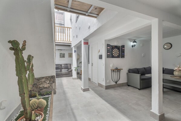 A spacious living area with a high ceiling, a cactus plant, a grey sofa, and a dartboard on the wall.