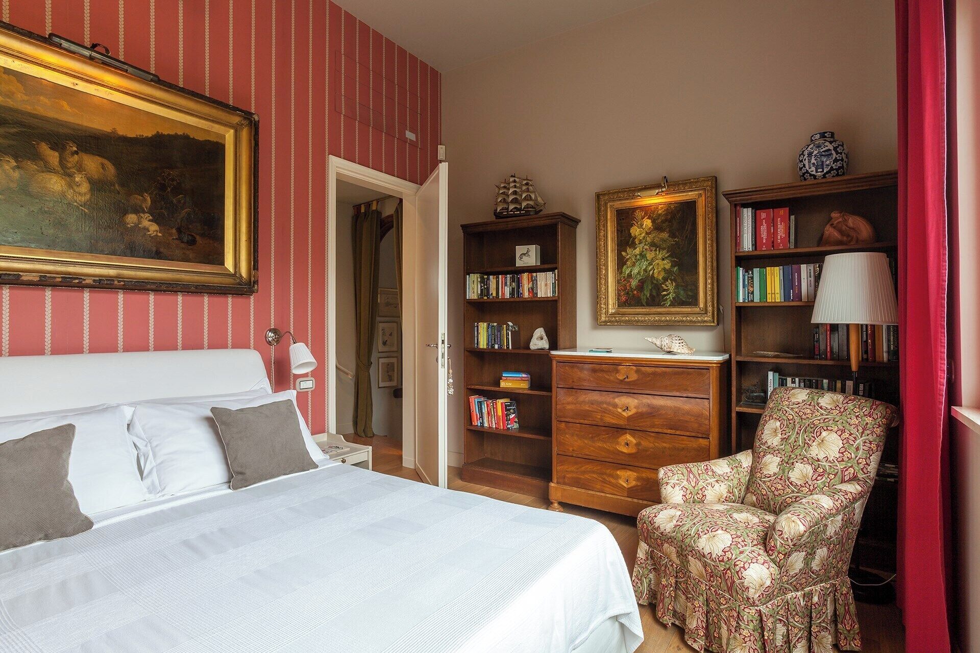 Ein Schlafzimmer mit einem Bett, einem Sessel, einem Bücherregal und einem Bild an der Wand.