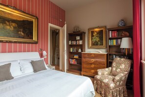 Ein Schlafzimmer mit einem Bett, einem Sessel, einem Bücherregal und einem Bild an der Wand.