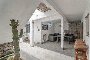 A spacious living area with a high ceiling, a stone wall, a cactus, and a dining area with a table and chairs. - Gran Canaria with Sea View, Shared Terrace, and Wi-Fi (Garachico)