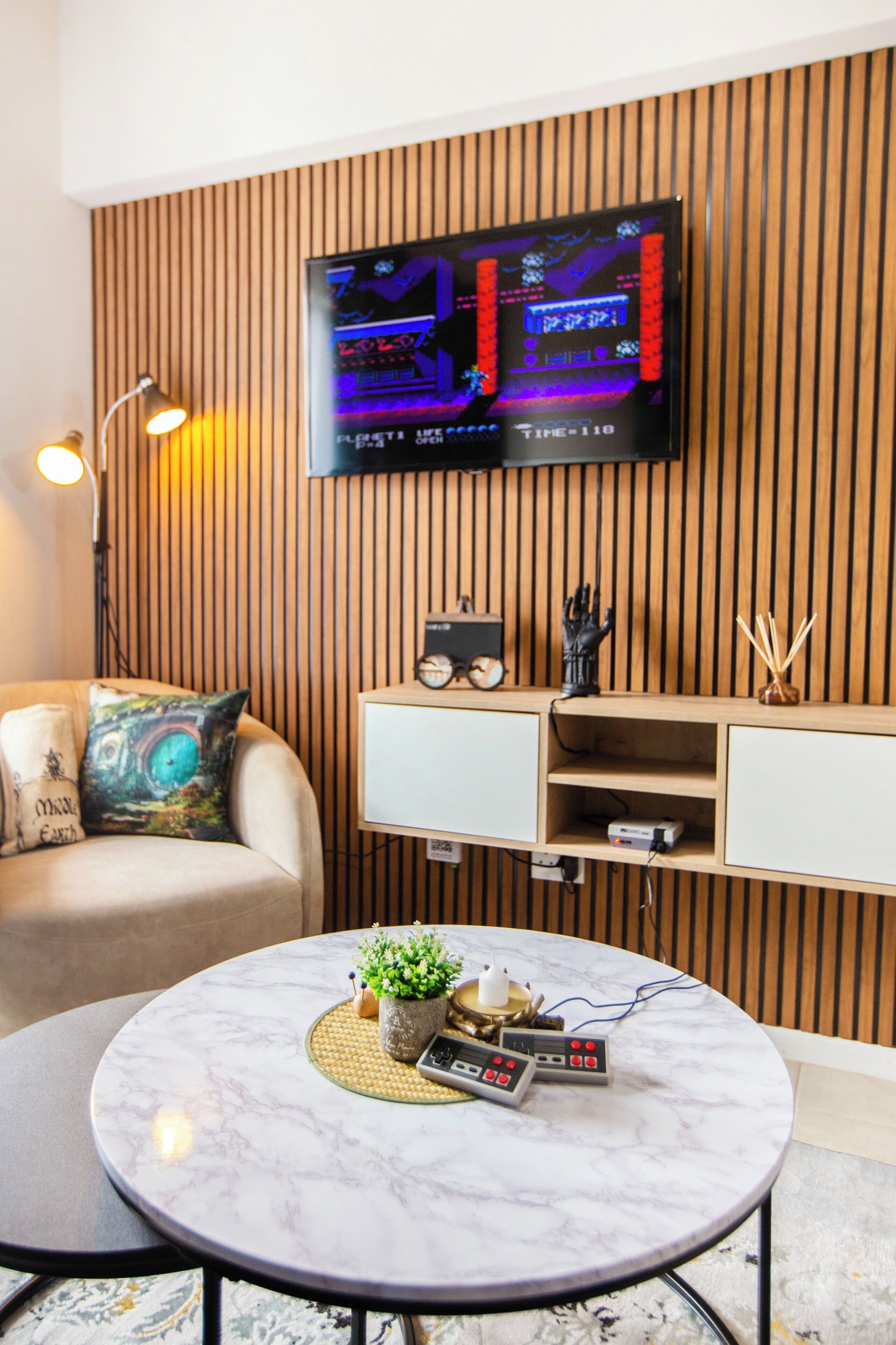 Ein modernes Wohnzimmer mit einem runden Marmor-Couchtisch, einer Couch mit Zierkissen, einem Wand-Fernseher und einer Wandverkleidung aus Holz.