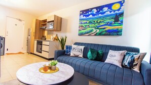 Uma sala de estar moderna com um sofá azul, uma mesa redonda e uma pintura de uma paisagem noturna.