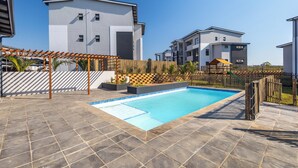 Uma área residencial moderna com piscina, pérgola de madeira e jardim cercado.