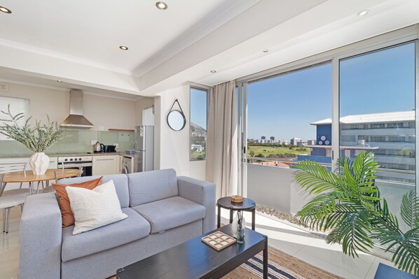 A modern living room with a grey sofa, a coffee table, and a view of a cityscape through large windows.