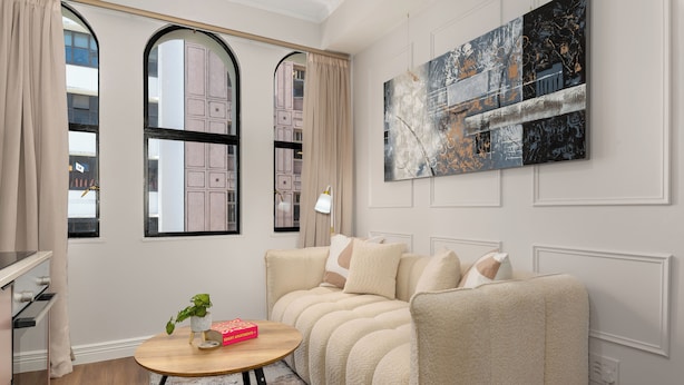 A modern living room with a beige sofa, a round wooden coffee table, and a large abstract painting on the wall.