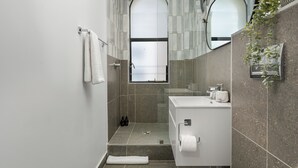 A modern bathroom with a shower, a sink, and a toilet. There are towels hanging on the wall and a plant on the counter.