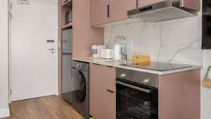 A compact kitchen with a washing machine, oven, and a coffee maker.