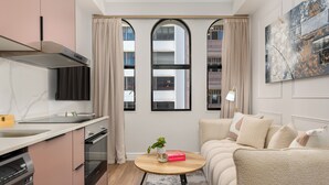 A modern kitchen with a built-in oven, a dining area with a round table, and a living space with a sofa and a painting on the wall.