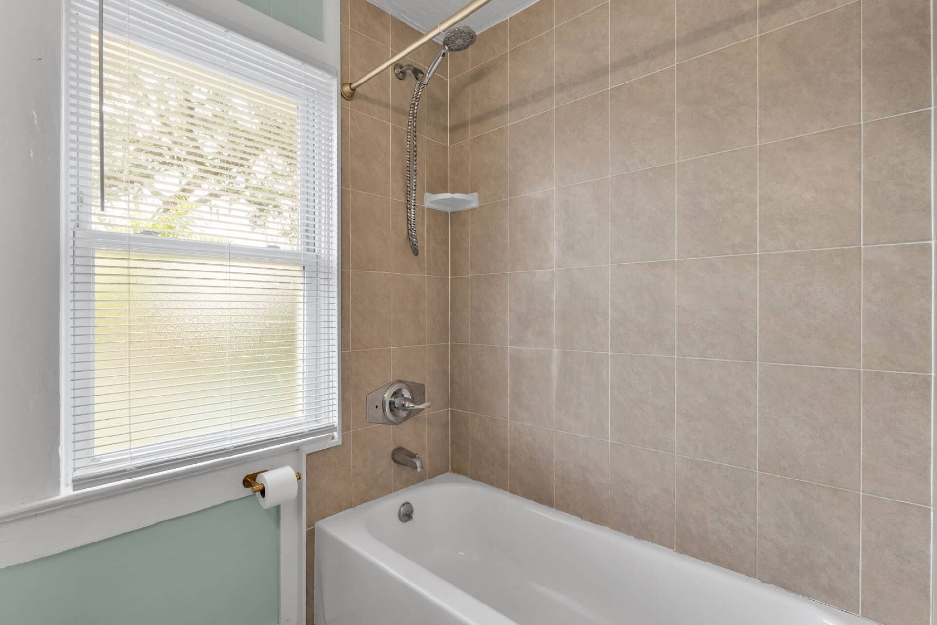 Een badkamer met een bad, douche en raam met zonwering.