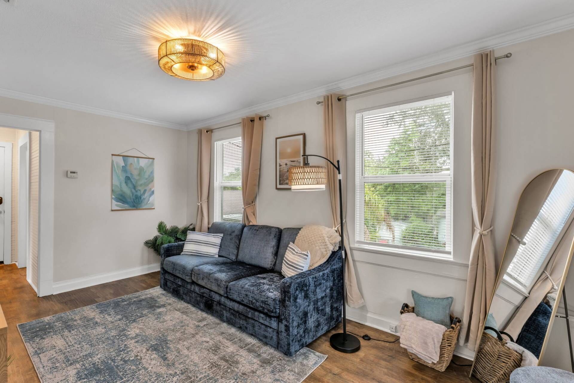 A living room with a blue sofa, a floor lamp, and a large window with curtains.