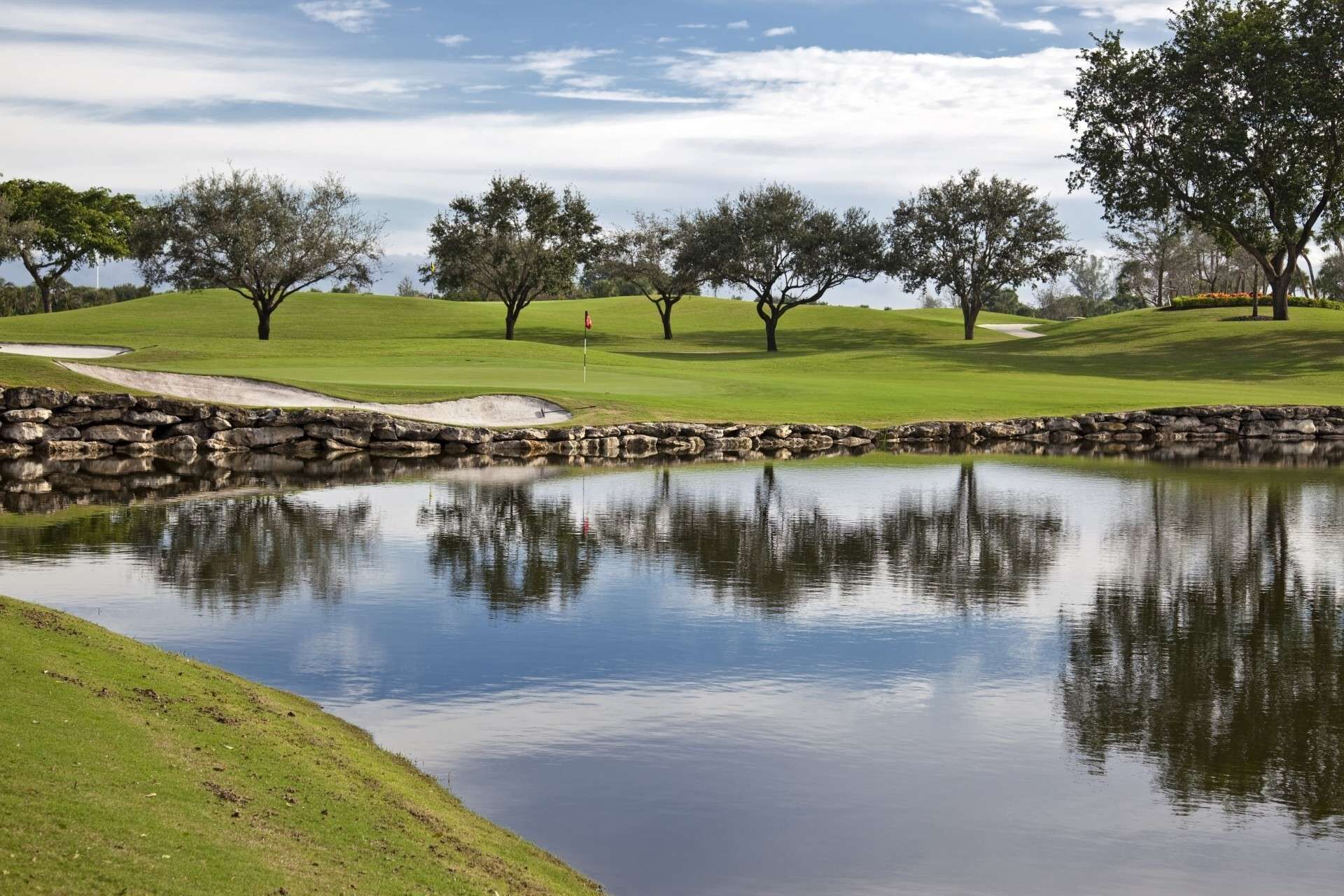 A serene golf course with a pond, stone walls, and trees.