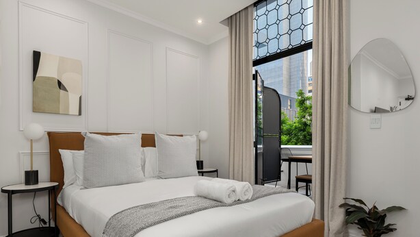 Ein modernes Hotelzimmer mit einem großen Bett, Blick auf die Stadt und einer Zimmerpflanze.
