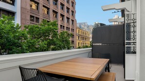 Ein Balkon mit Holztisch und Stühlen, mit Blick auf eine Stadtlandschaft aus Gebäuden und Grünflächen.