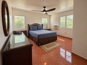 Ein Schlafzimmer mit einem Bett, einem Schminktisch, einem Deckenventilator und Fenstern mit Jalousien.