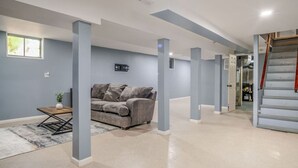 Un amplio espacio de sala con un sofá gris, una mesita con un florero, y una escalera a la derecha.