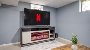 Una sala de estar con un televisor de pantalla plana montado en un mueble bajo de madera, una chimenea debajo del televisor y una mesita con una planta.