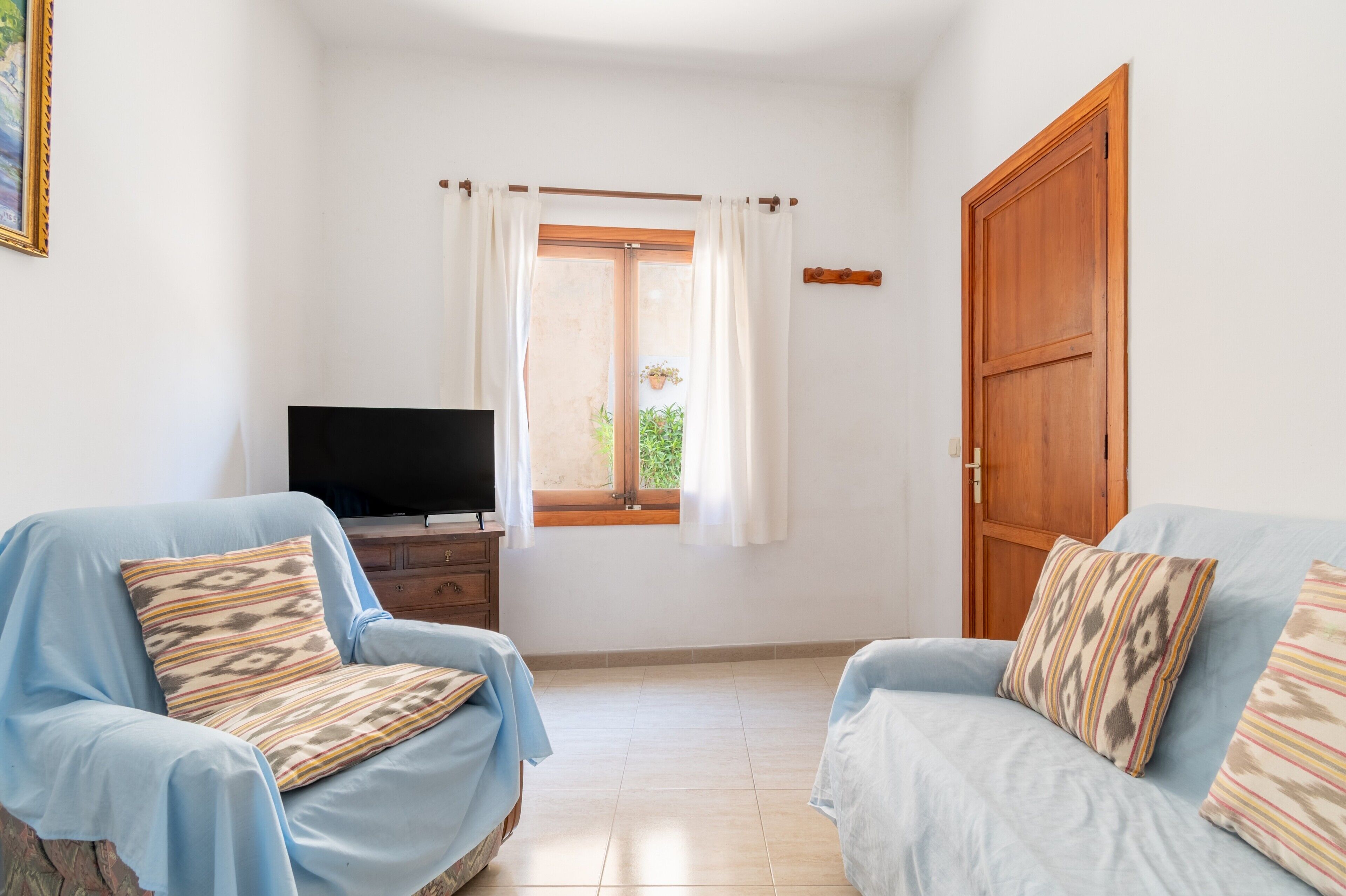 A room with two light blue sofas, a wooden door, a television on a wooden cabinet, and a window with curtains.