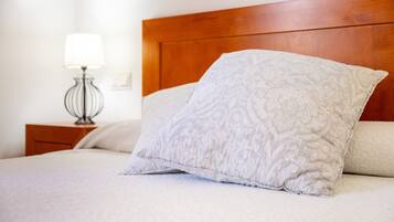 A neatly made bed with a wooden headboard, a bedside lamp, and a patterned pillow.