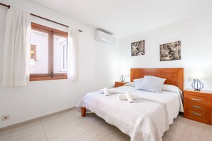 Ein Schlafzimmer mit Bett, Fenster mit Vorhängen, Nachttisch und Wandbild.