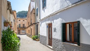 A narrow street with buildings on either side, a door with a sign, and potted plants. - Holiday Home 'Casa Guillermo' with Mountain View, Wi-Fi and Air Conditioning (Pollensa)