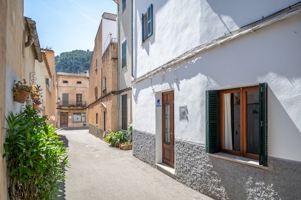 A narrow street with buildings on either side, a door with a sign, and potted plants.
