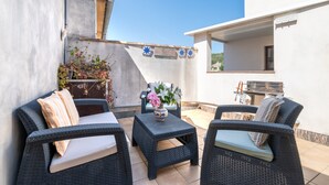 A patio with wicker furniture, a small table with a vase, and a grill area. - Holiday Home 'Casa Guillermo' with Mountain View, Wi-Fi and Air Conditioning (Pollensa)