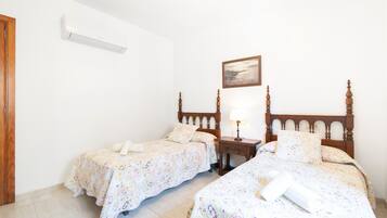 Habitación de hotel con dos camas individuales, cabecero de madera, mesita de noche con lámpara y un cuadro en la pared.