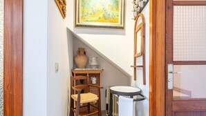 A narrow hallway with a wooden door, a small table with a vase and pitcher, a chair, and a radiator. - Holiday Home 'Casa Guillermo' with Mountain View, Wi-Fi and Air Conditioning (Pollensa)