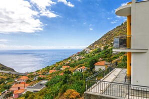 Un quartier résidentiel situé sur la côte, avec des maisons construites sur une colline, un ciel dégagé et une vue sur la mer.