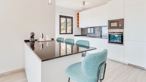 Una cocina moderna con armarios blancos, encimera negra y sillas color turquesa.