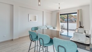 Un comedor moderno con una mesa de vidrio, sillas color turquesa y vistas a una zona residencial a través de grandes ventanales.