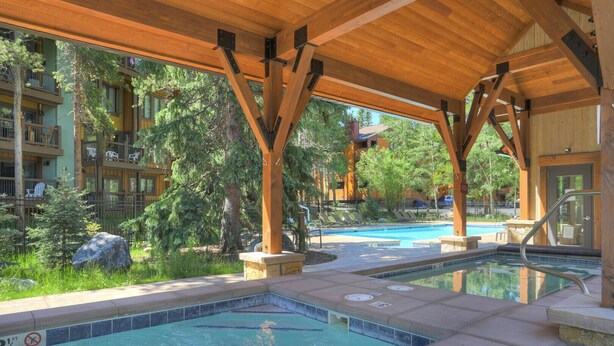 A pool area with wooden beams, lounge chairs, and a view of a building with balconies. - Stunning Mtn Condo - Prime Location, Walk to Ski Lifts & Main Street! (Breckenridge)