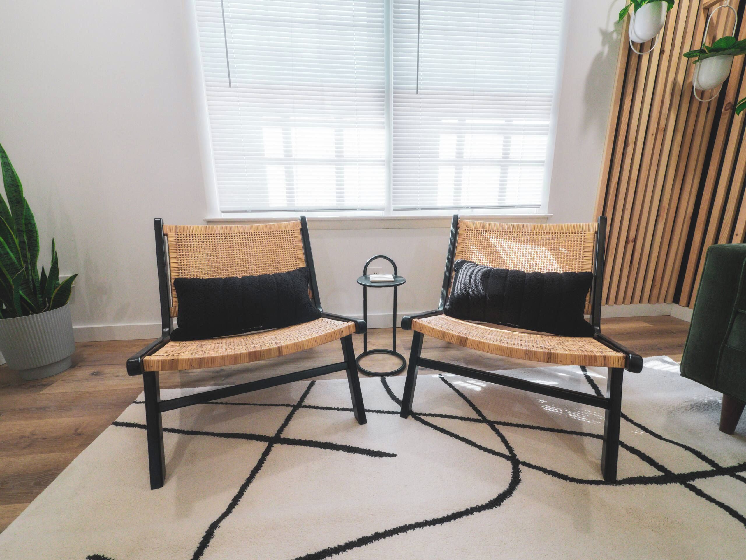 Two wicker chairs with black cushions, a small table, and a potted plant in a corner.